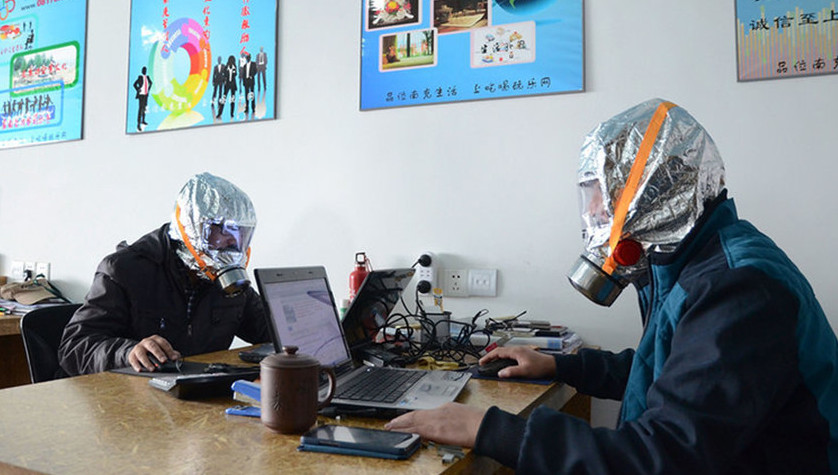 [IMG: Men in gas masks at computers]